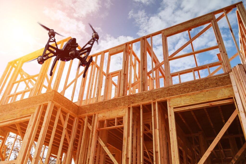 Black drone quadcopter with camera flying over residential construction home framing against a blue sky. Roofing construction. Wooden construction