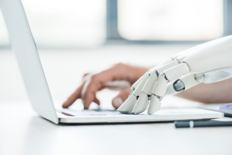 Caption selective focus of human and robot hands typing on laptop at workplace Description